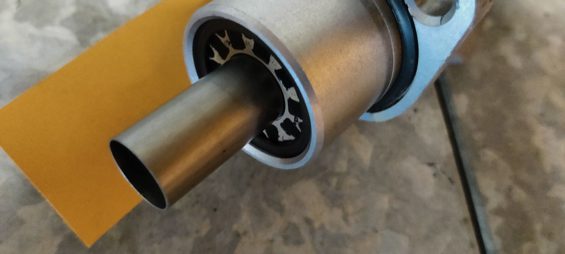 Een gebruikte hoofdremcilinder van een auto met een wit plastic vloeistofreservoir, staand op een grijze betonnen ondergrond.