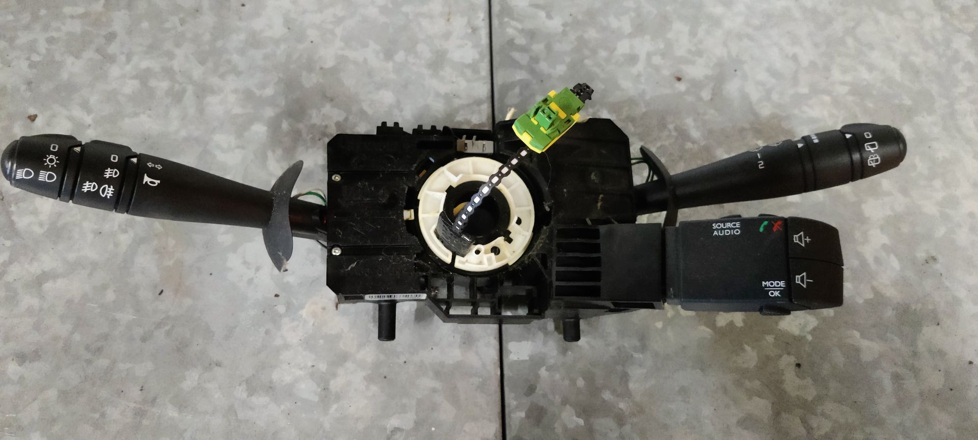 Een zwarte stuurkolomschakelaarunit voor auto's met richtingaanwijzer- en ruitenwisserhendels en een centrale klokveermodule.