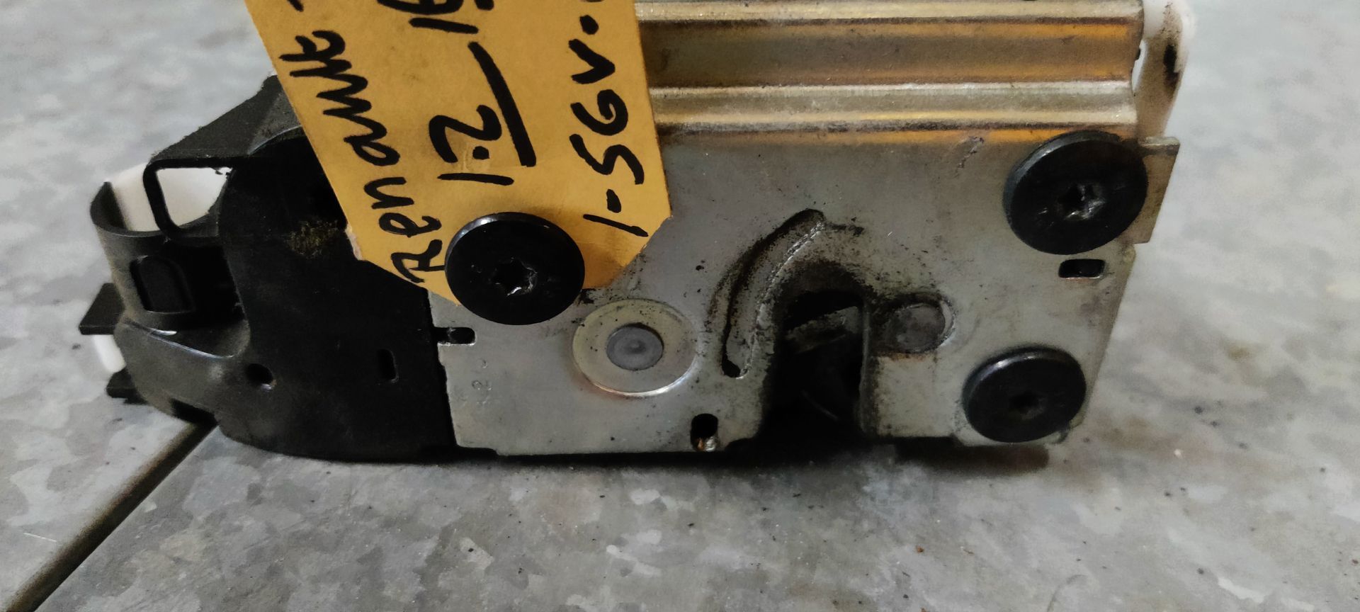 Een deurslotmechanisme van een Renault-voertuig met een geel identificatielabel, rustend op een grijze tegelondergrond.