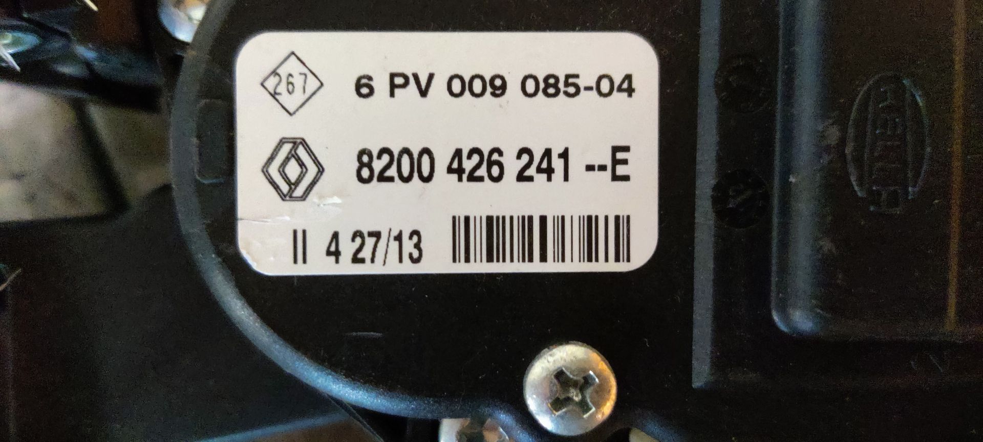 Een zwart elektronisch gaspedaal voor een voertuig met een geel identificatielabel op een grijs oppervlak.