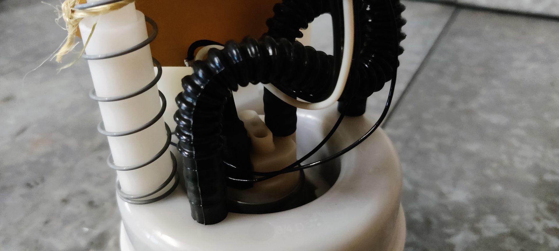 Een gebruikte brandstofpompunit voor auto's met een losse rechthoekige sensor, staand op een grijze betonnen ondergrond.