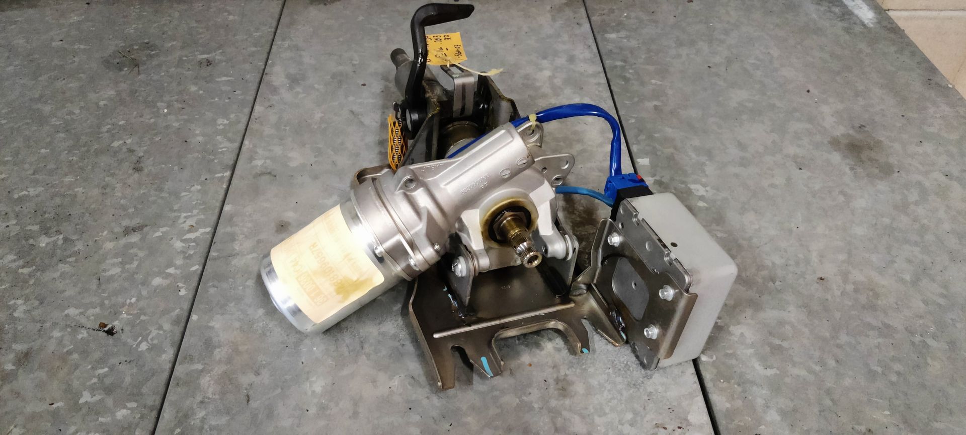 Een elektrische stuurbekrachtigingsmotor voor auto's met bijbehorende regelmodule, gelegen op een grijze werkbank.