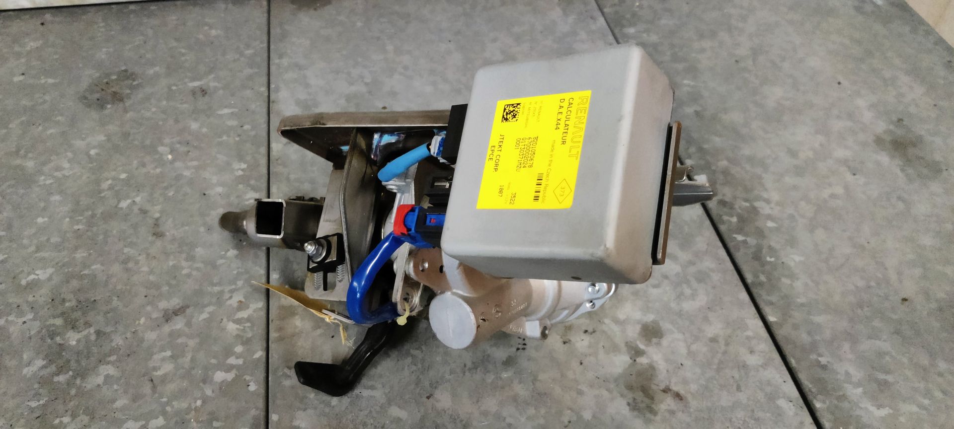 Een elektrische stuurbekrachtigingsmotor voor auto's met bijbehorende regelmodule, gelegen op een grijze werkbank.