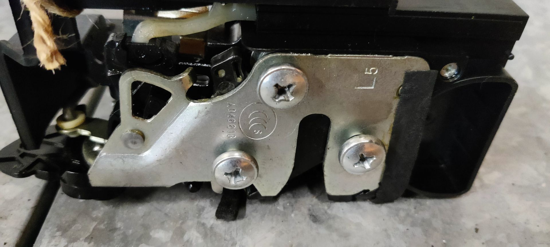 Een autodeurvergrendeling met twee aangesloten kabels, geplaatst op een grijs metalen oppervlak.