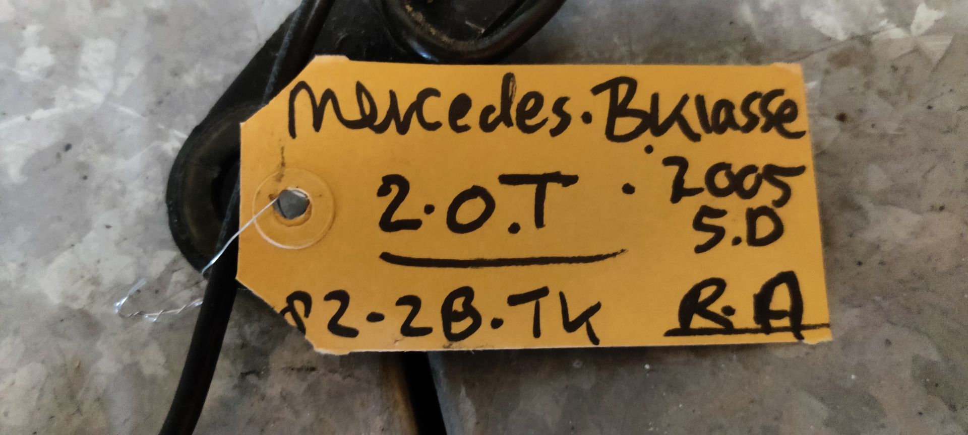 Een zwarte autogordelgesp met een gele elektrische connector en een handgeschreven identificatielabel.