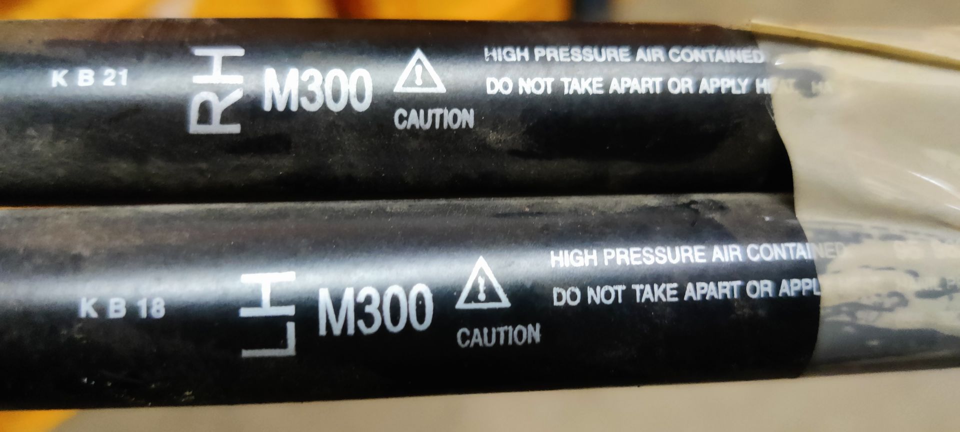 Een aandrijfas met twee kruiskoppelingen, omwikkeld met beschermend papier en tape, ligt op een grijze ondergrond.