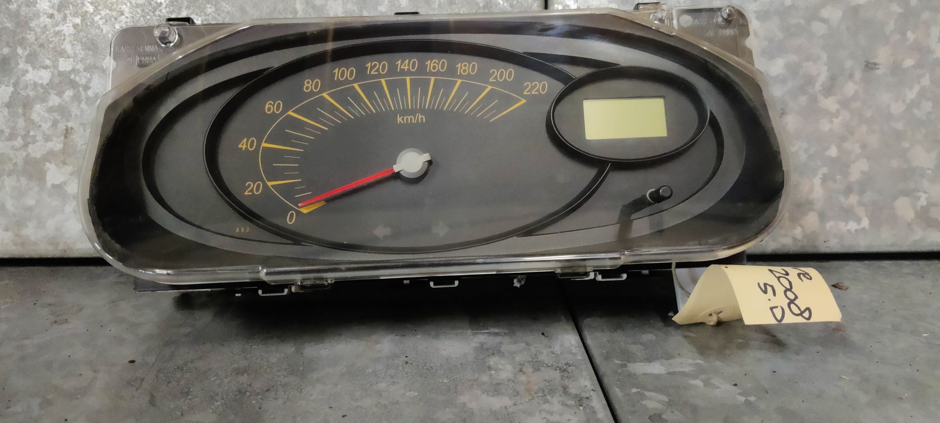 Een ronde snelheidsmeter voor auto's met een zwarte wijzerplaat, witte markeringen en een rode wijzer op een metallic achtergrond.