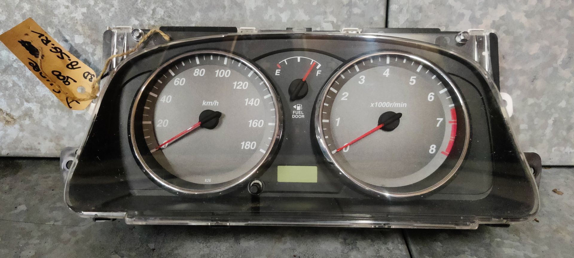 Een instrumentenpaneel voor auto's met twee grote analoge meters, een centraal digitaal display en een aangehecht papieren label.