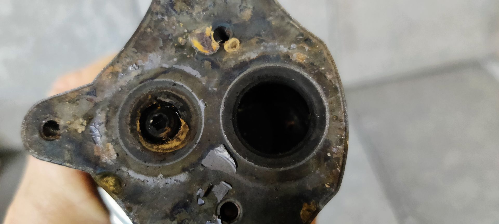 Close-up van een vuile, metalen waterpomphuis voor auto's, waarop ronde openingen te zien zijn met tekenen van corrosie en aanslag.