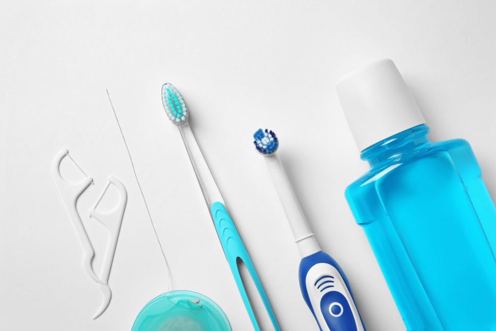 A Toothbrush, Mouthwash, Floss And Toothpaste On A White Surface — Aspire Dental in Townsville, QLD