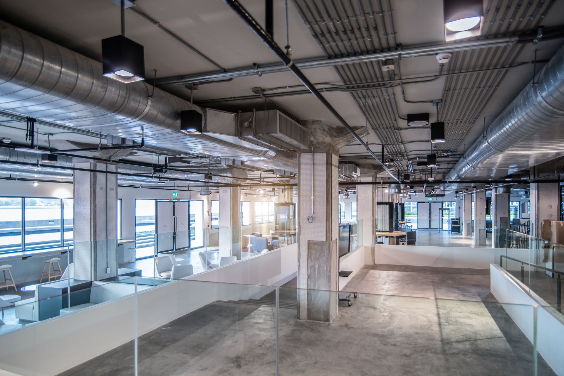 Empty modern office interior with exposed ceiling, glass walls, and concrete floors