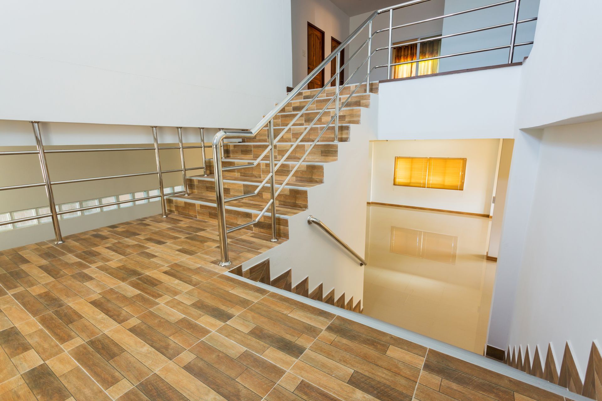 Staircase with tiled steps and metal railings, leading to a second floor with white walls and natural light Staircase with tiled steps and metal railings, leading to a second floor with white walls and natural light