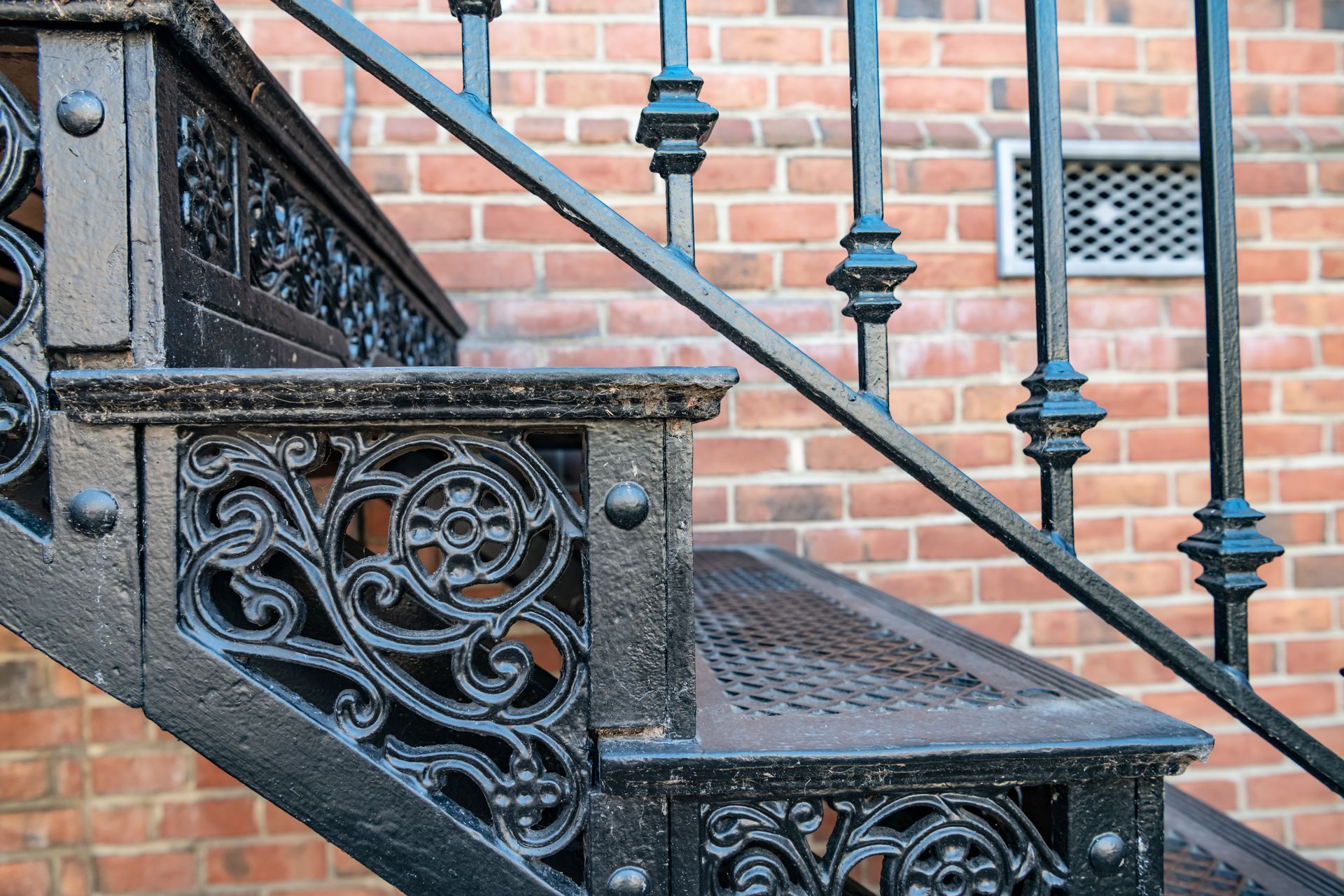 Black metal staircase with ornate railing against a red brick wall