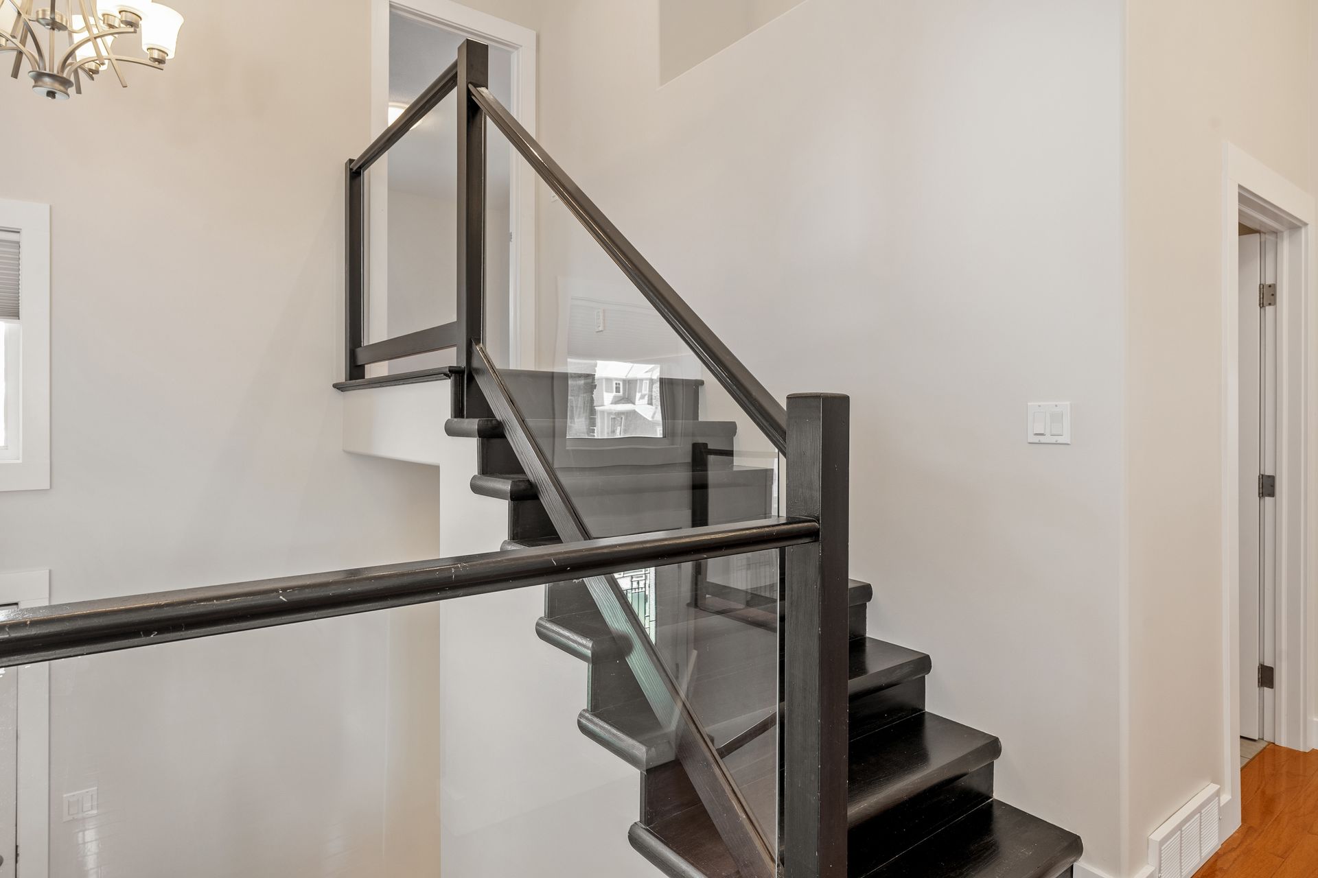Staircase with dark wood steps and railing, glass panels, and white walls Staircase with dark wood steps and railing, glass panels, and white walls