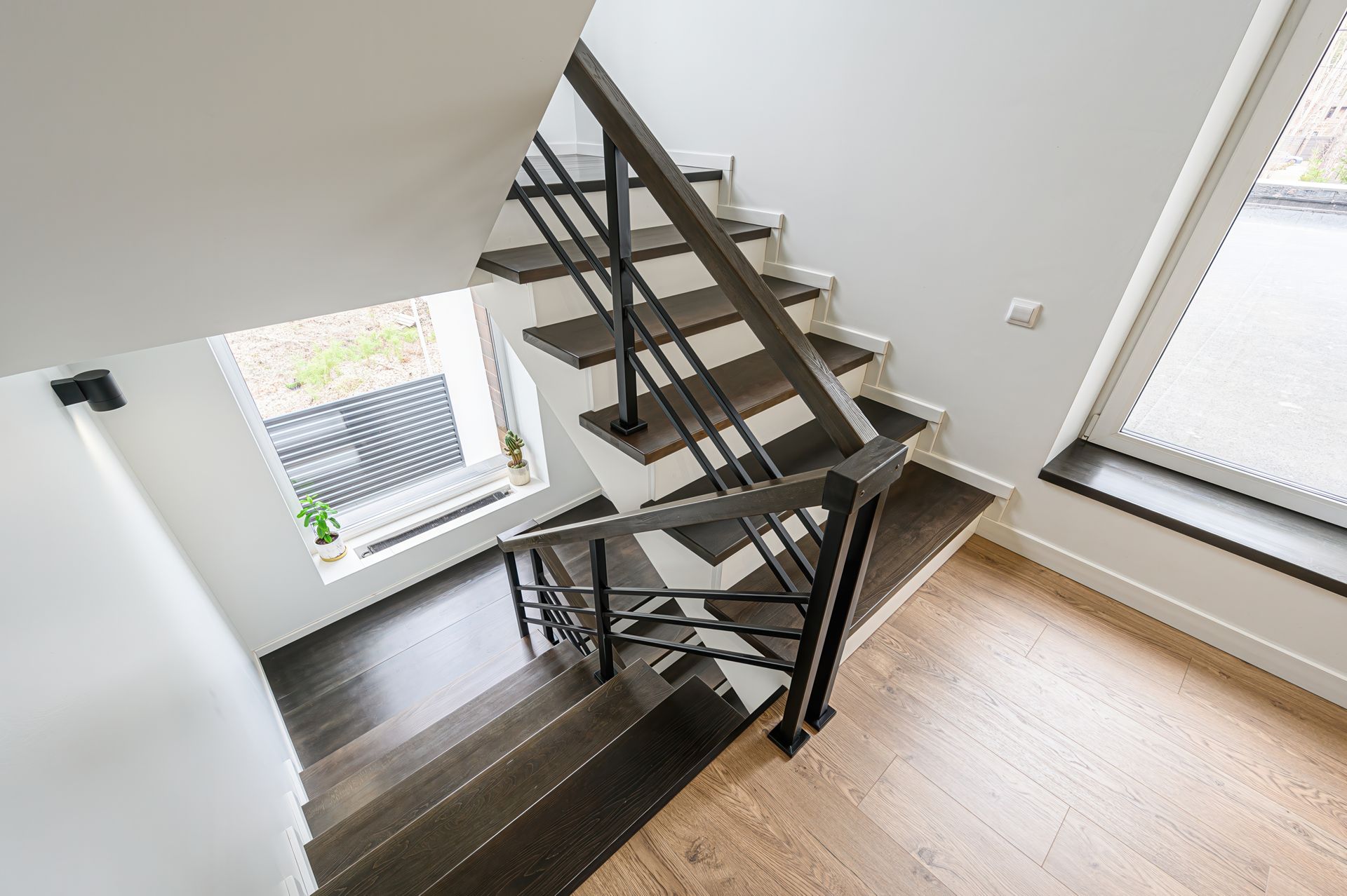 Staircase with dark wooden steps, black metal railing, white walls, and a window Staircase with dark wooden steps, black metal railing, white walls, and a window