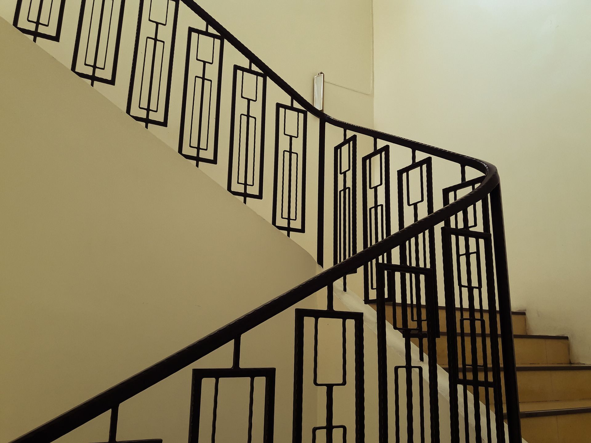 Black iron railing on a curved staircase with beige walls and light brown steps Black iron railing on a curved staircase with beige walls and light brown steps