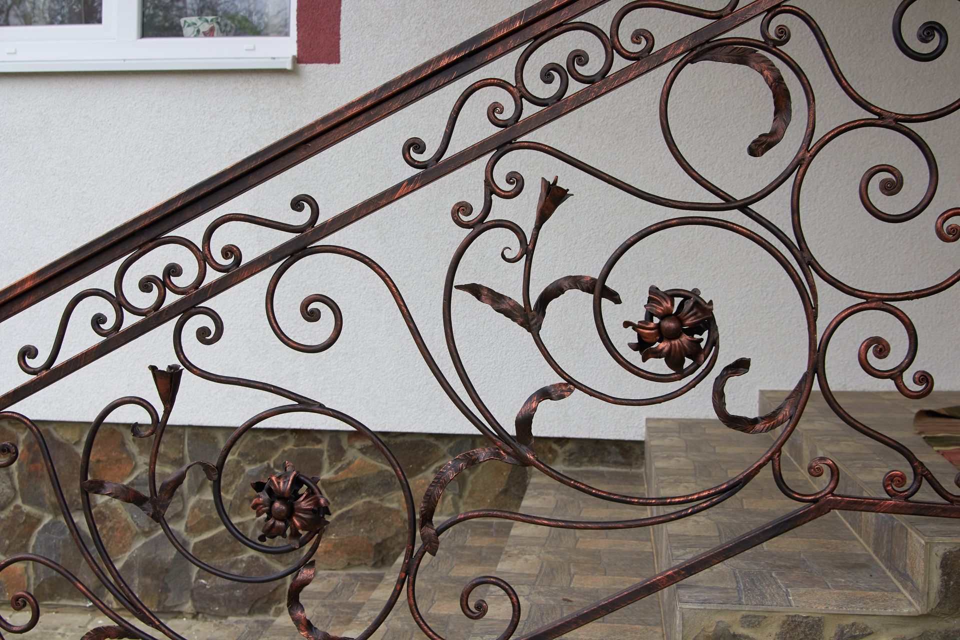 Ornate wrought-iron railing with floral and swirl designs, painted brown, next to outdoor stone steps