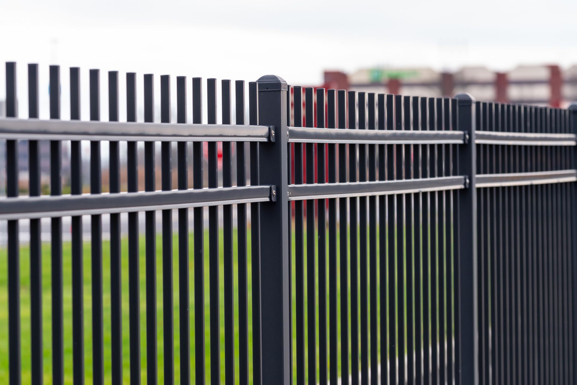 Black metal fence with vertical bars, green grass, and a building in the background
