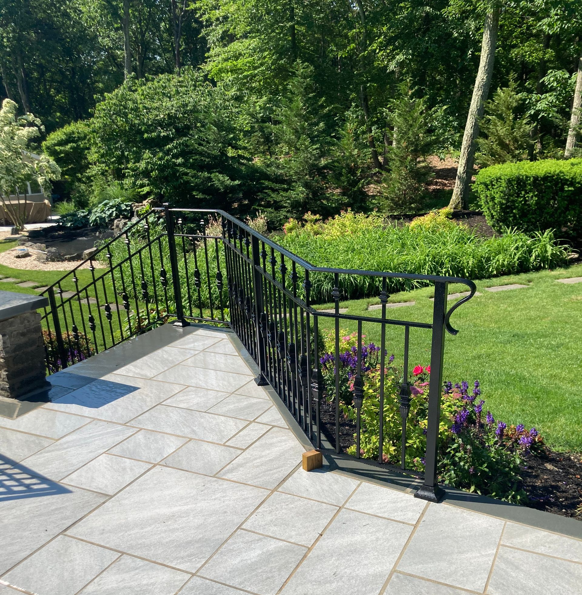 Decorative black wrought-iron fence with beige pillars and a concrete base, in front of greenery and buildings Decorative black wrought-iron fence with beige pillars and a concrete base, in front of greenery and buildings