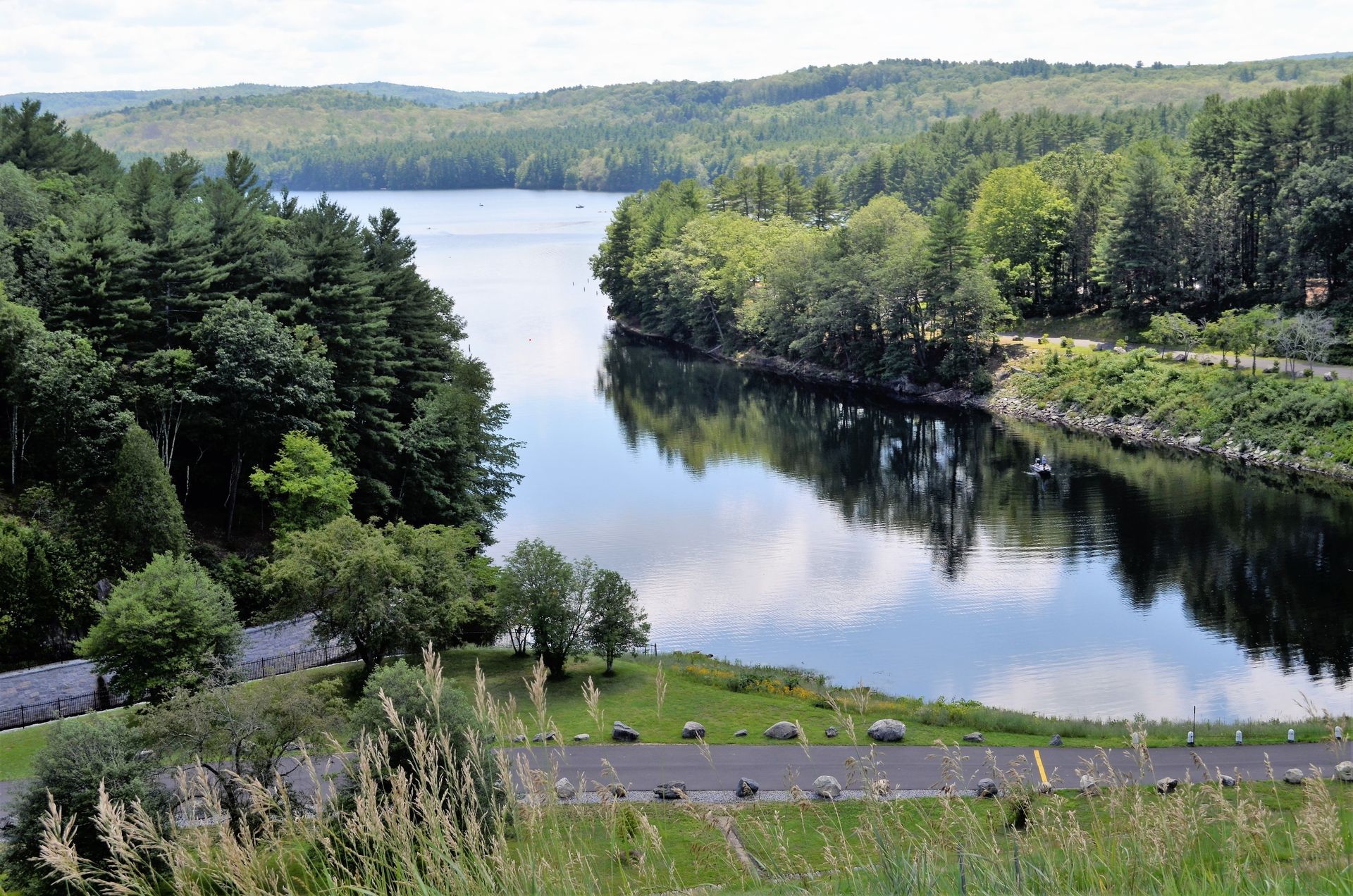 Calm lake surrounded by lush green trees and rolling hills under a bright sky.