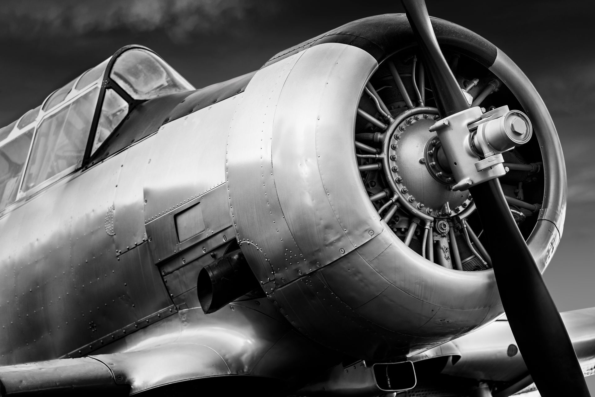 Close-up of a vintage airplane's silver metal fuselage, propeller, and cockpit in black and white.
