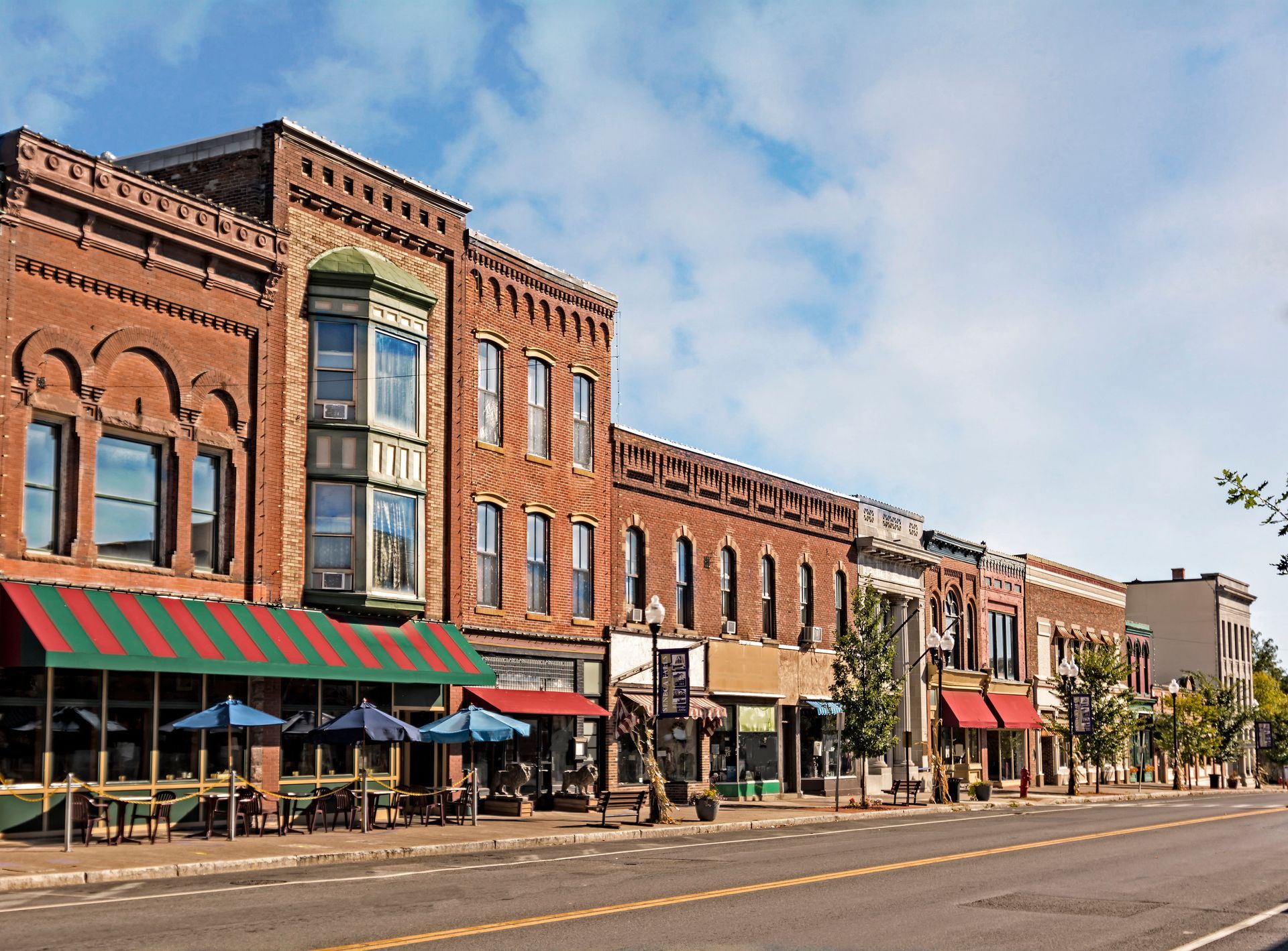 Row of brick storefronts on a sunny street, featuring awnings and potential outdoor seating.