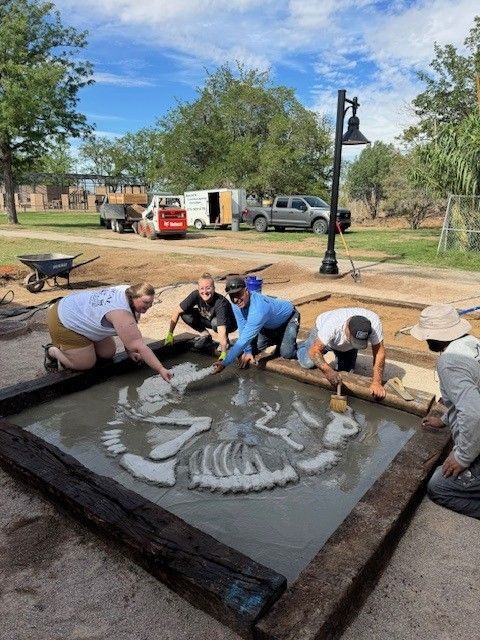 People excavating fossilized bones in a square pit outdoors.
