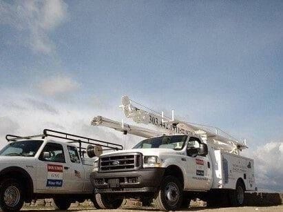 Two utility trucks are parked next to each other on a road.