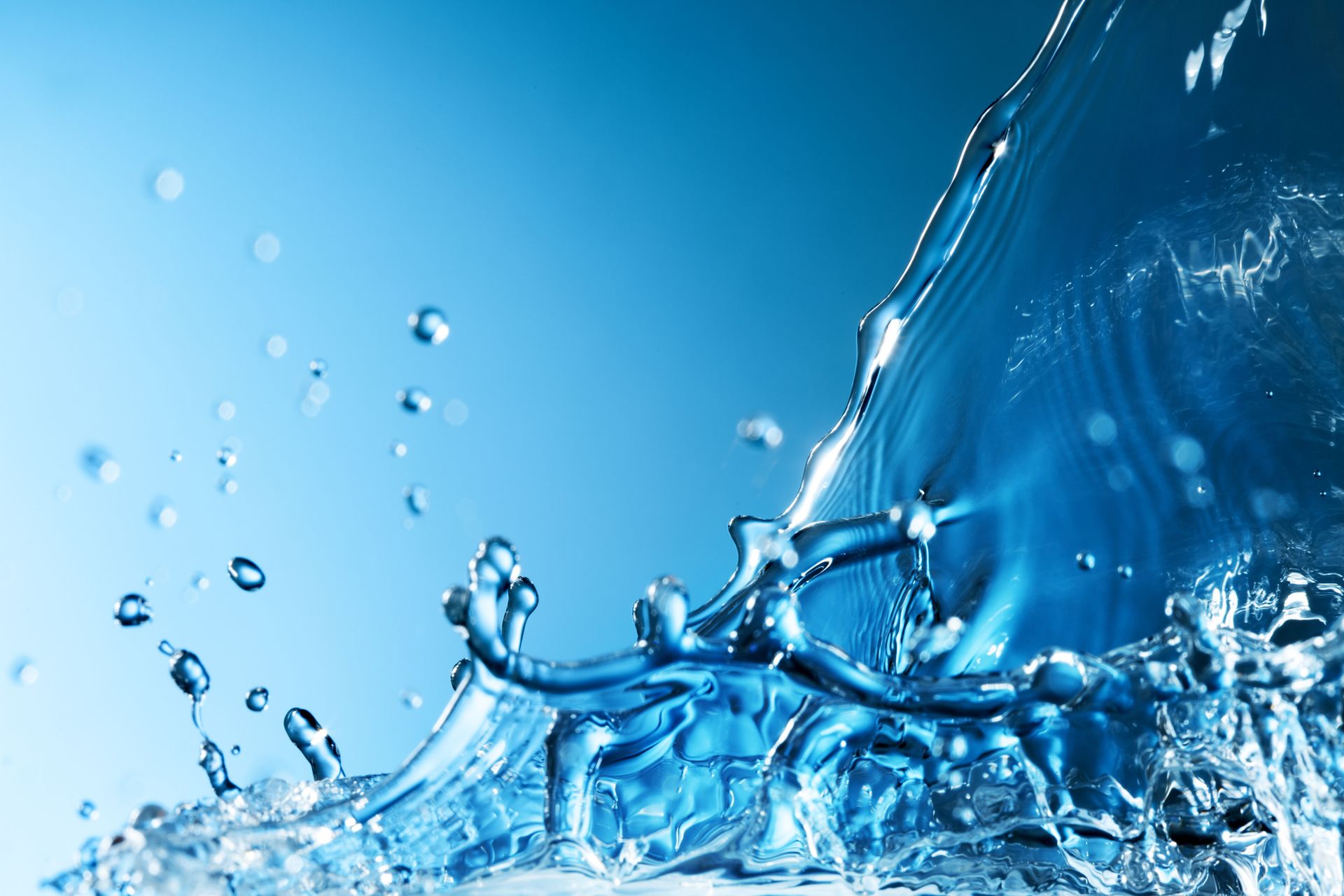 Splash of clear blue water with droplets against a light blue gradient background.
