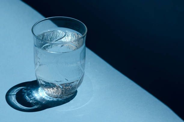 A glass of water casting a shadow on a blue surface, illuminated by light.