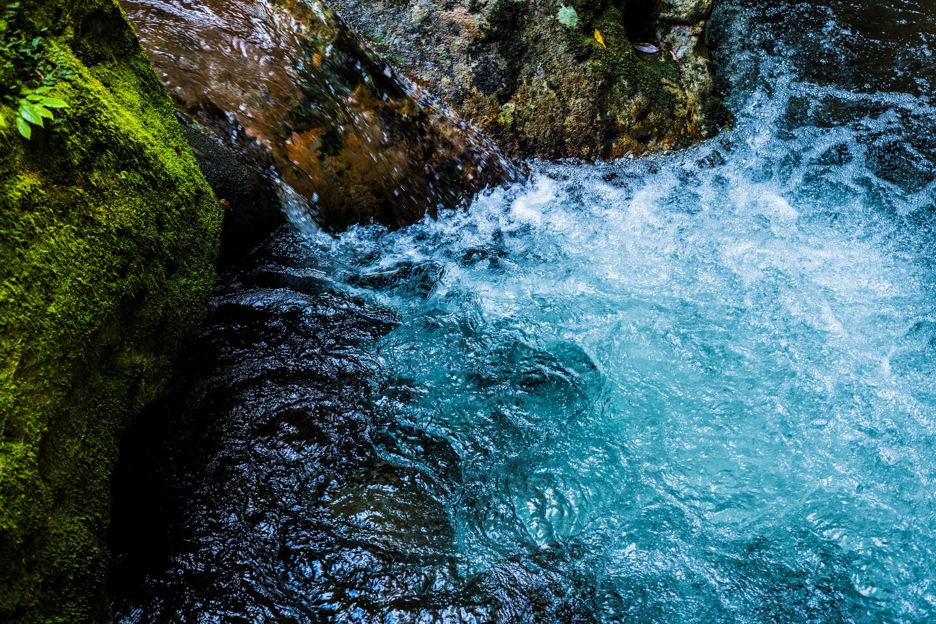 Rushing turquoise water cascades over mossy rocks.