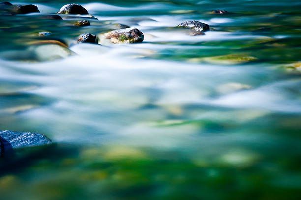 Blurred water flowing over rocks in a stream. Emerald and blue hues create a serene, natural scene.