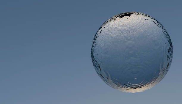 Water sphere suspended against a clear blue sky, reflecting light and ripples on its surface.