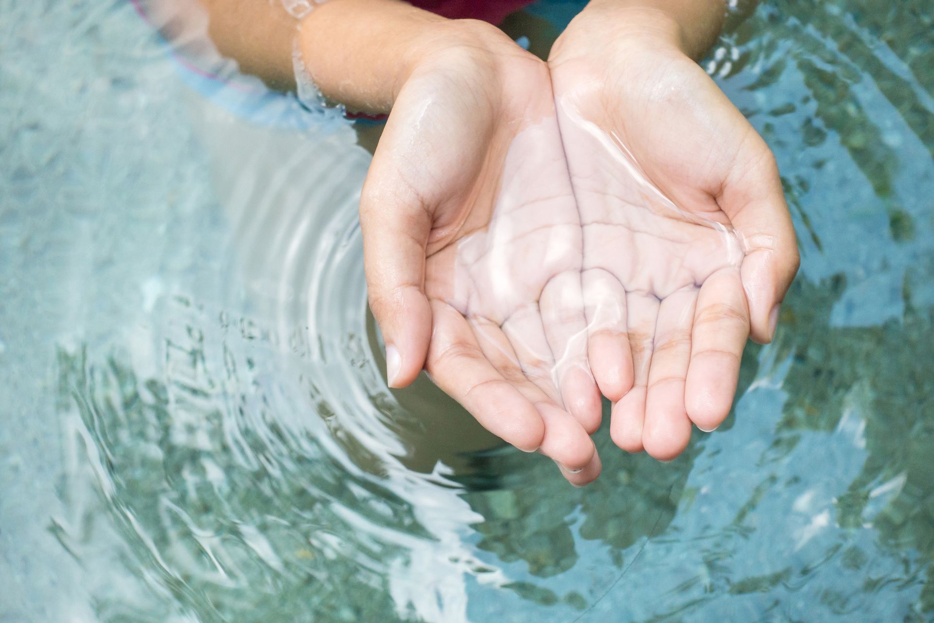 Person's cupped hands holding water in a pool. Clear water and rippling surface.