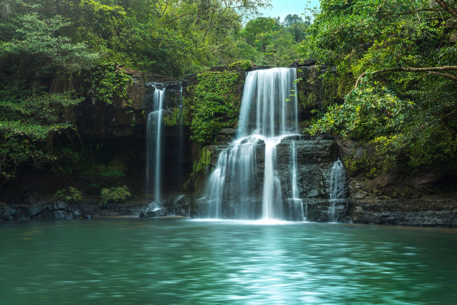 A waterfall is surrounded by trees and a body of water.