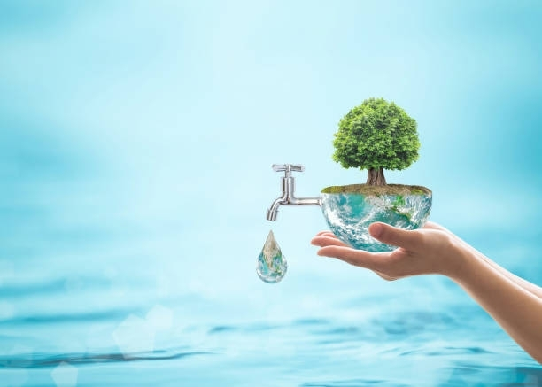 Hands holding a miniature earth with a tree, water faucet, and a water droplet. Blue water background.