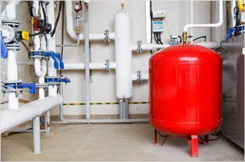 There is a red tank in the middle of a room with pipes.
