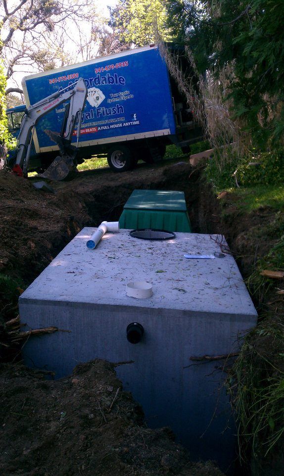 Concrete septic tank in a trench, next to a green lid and blue truck.