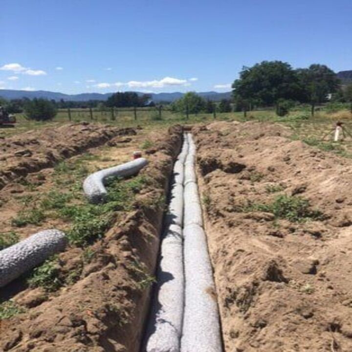 Two long trenches with cylindrical filter socks for drainage in a field; sunny day.