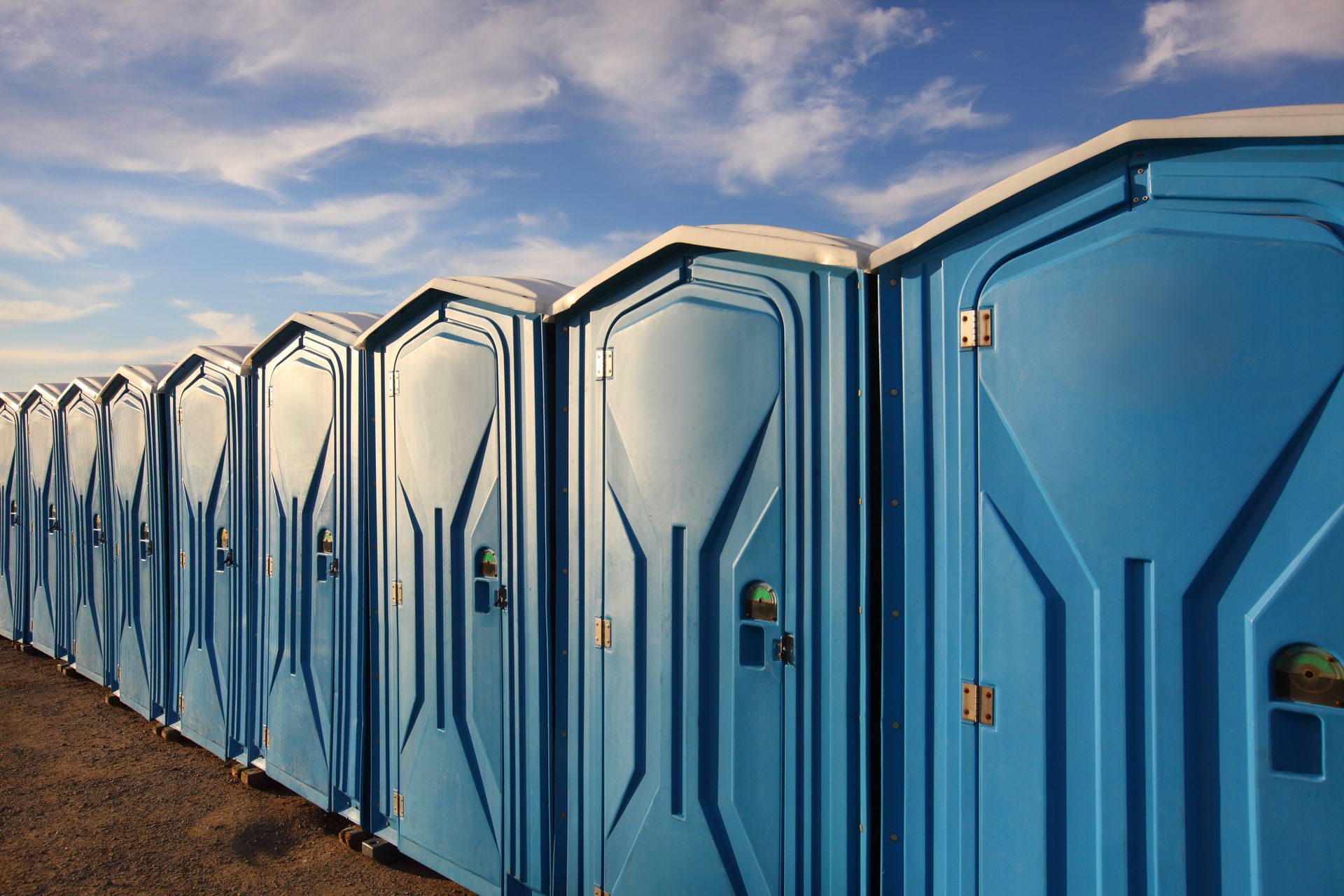 Row of blue portable toilets against a partly cloudy sky.