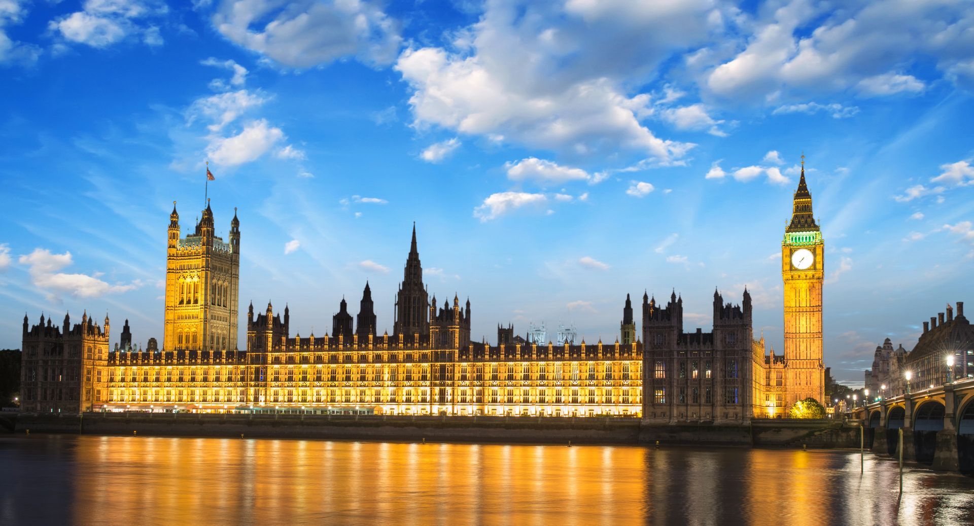 View of the UK Parliament looking across the River Thames alongside Westminster Bridge at dusk