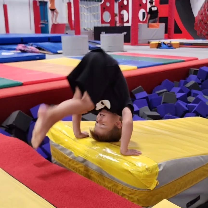 Person doing a handstand on a yellow mat in an indoor gymnastics foam pit