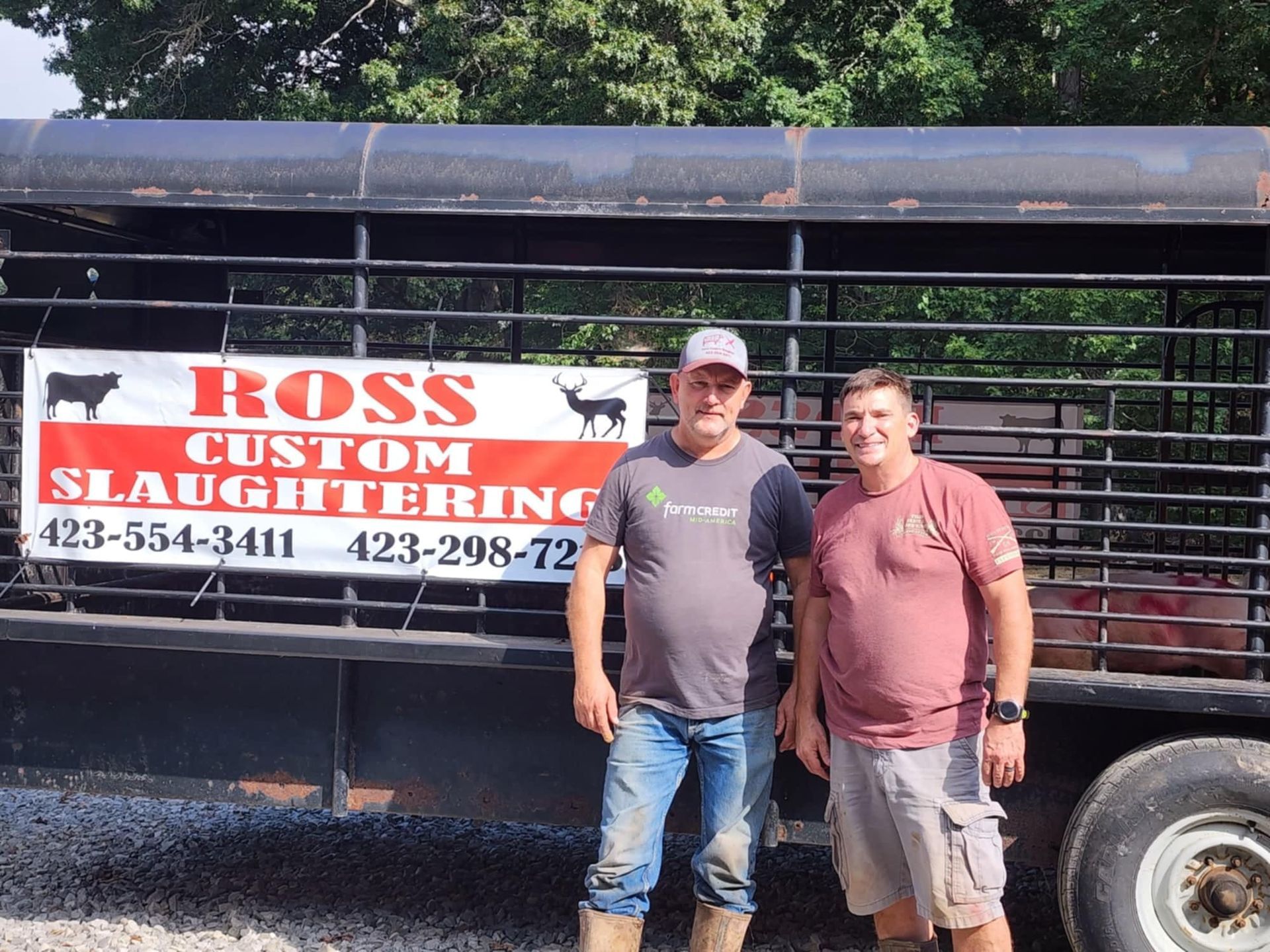 Two men stand in front of a trailer with a