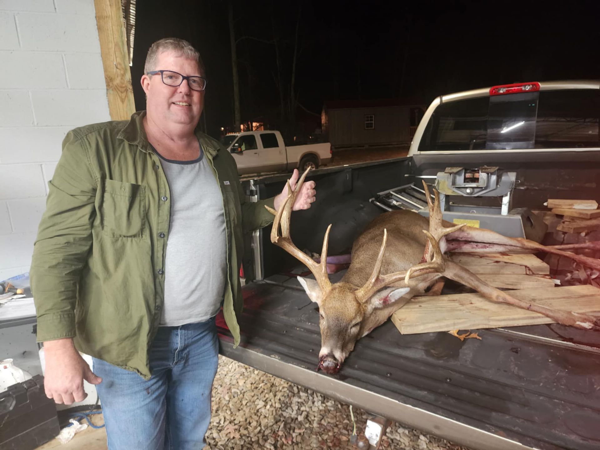 Man with a large buck deer in the back of a truck, giving a thumbs up.