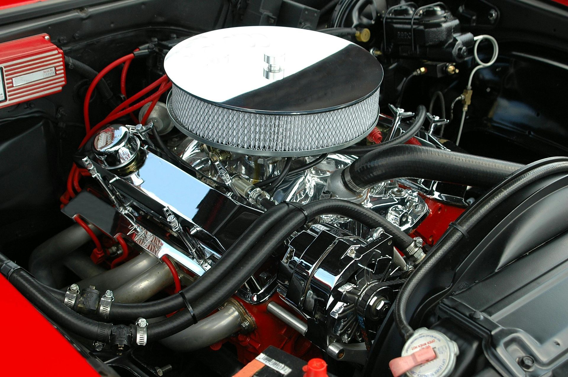 Chrome engine in a red car, air filter, and black hoses.