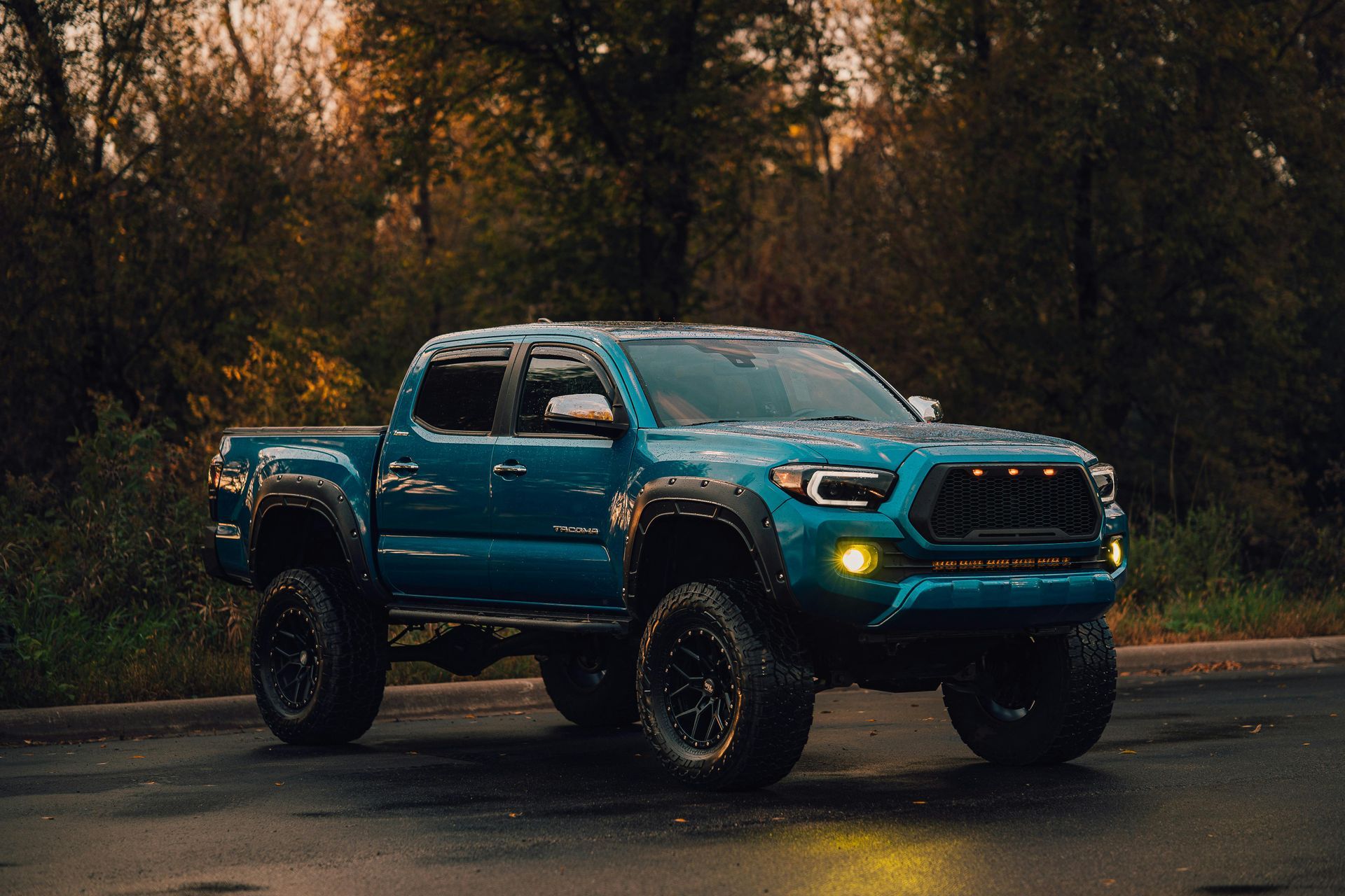 Teal lifted Toyota Tacoma truck, black wheels, forest background.