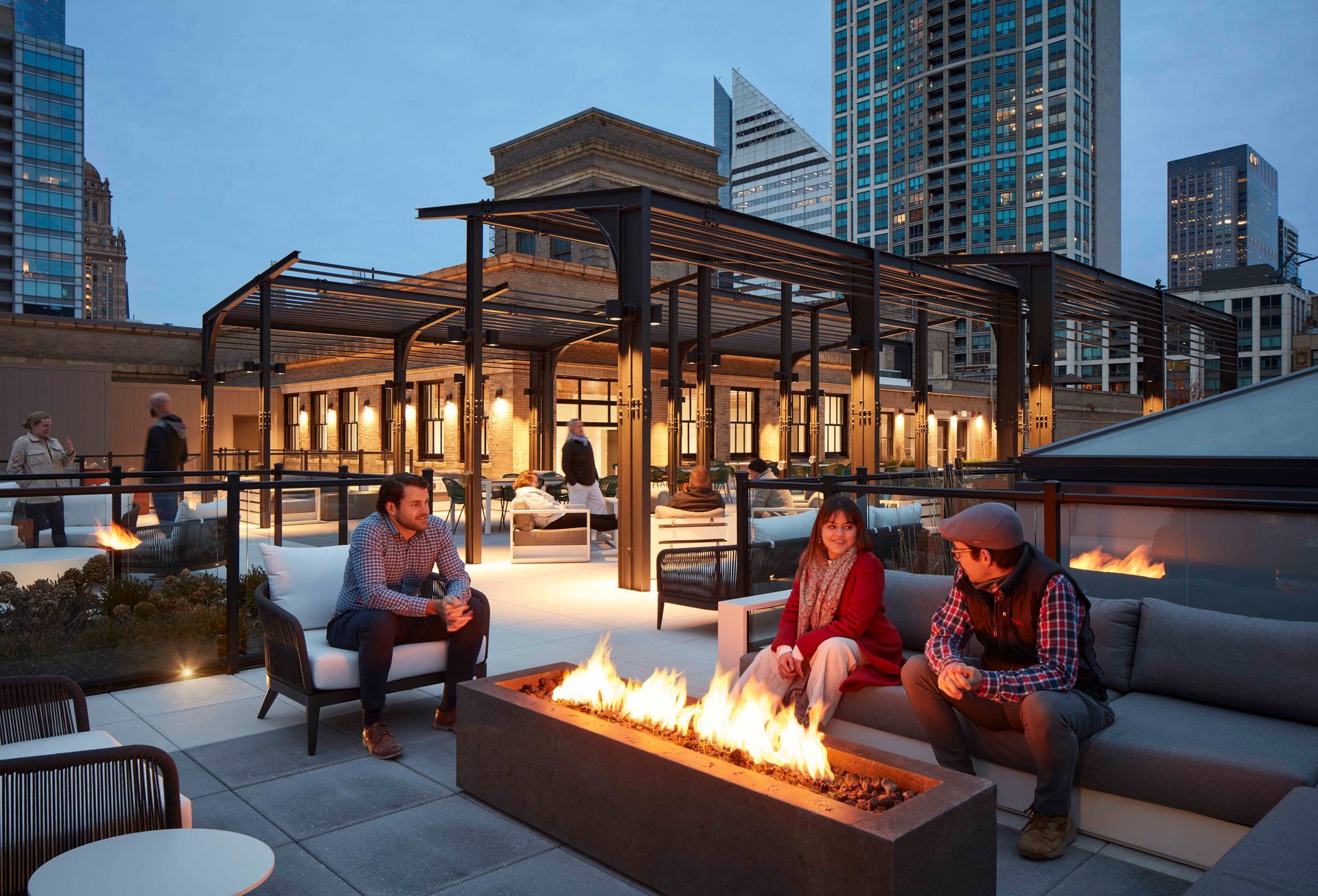 A group of people are sitting around a fire pit on a rooftop