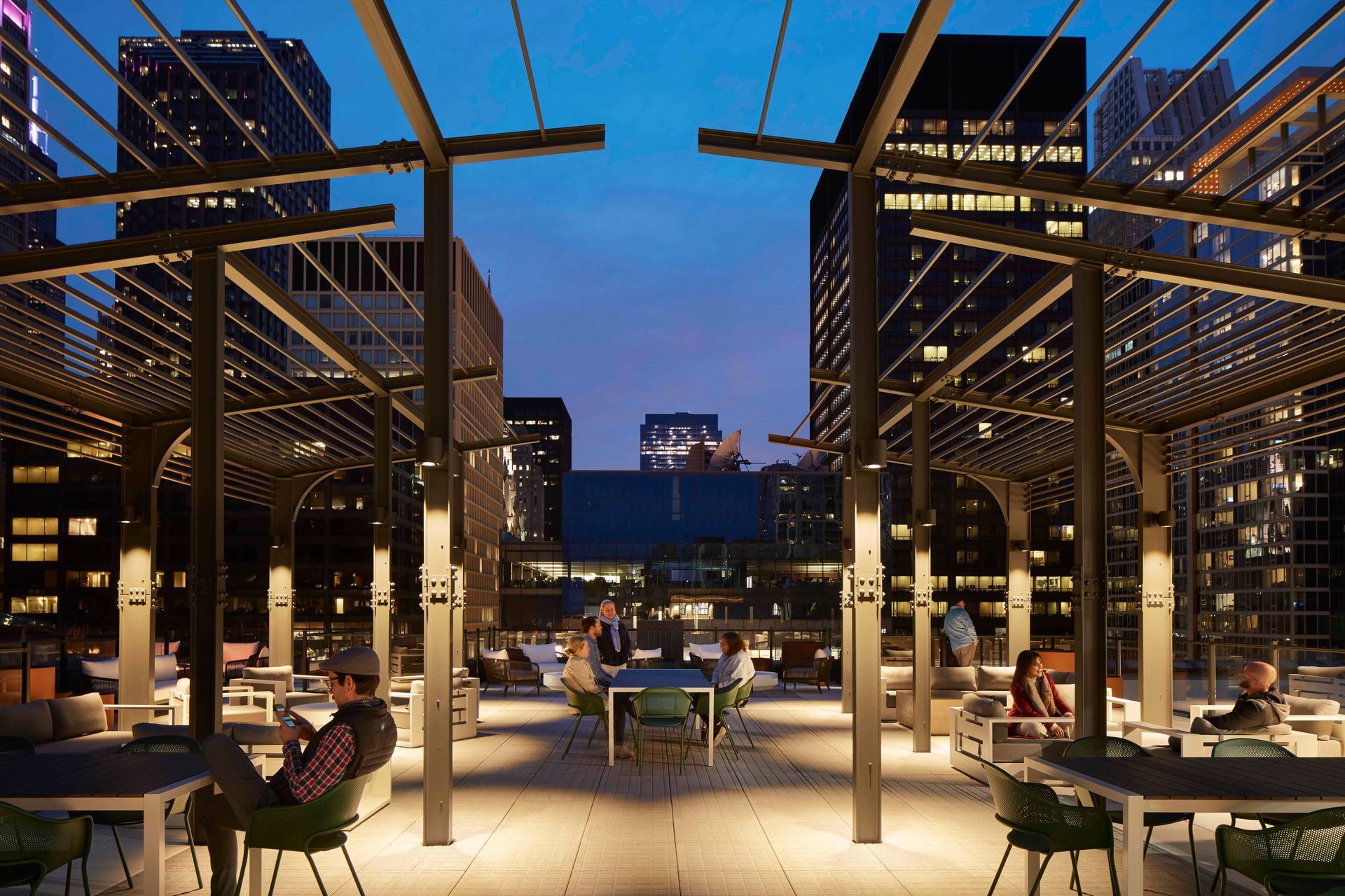A group of people are sitting at tables under a pergola.