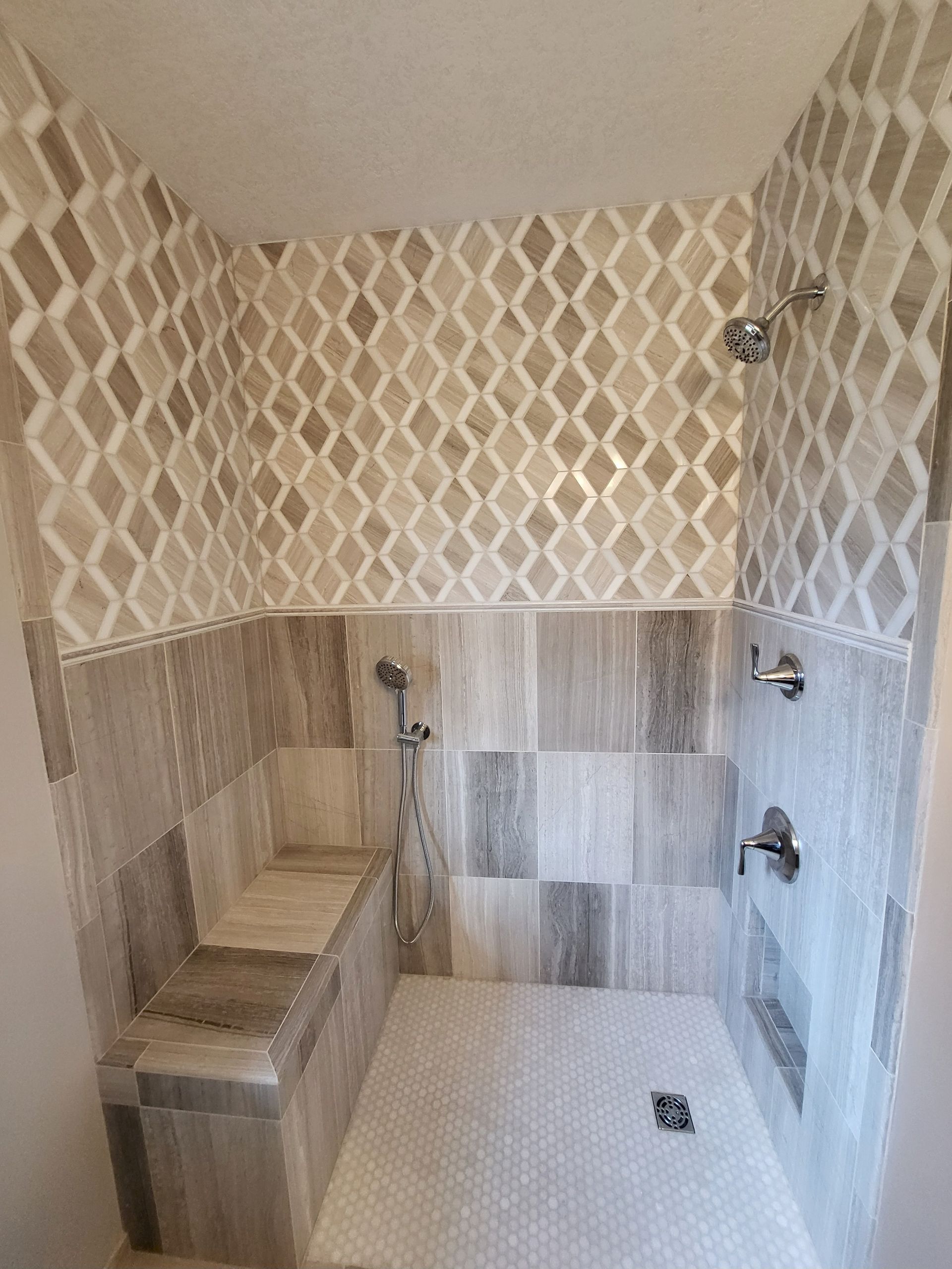 Tiled shower with a bench seat. Features diamond-patterned tile above wood-look tile, with silver fixtures against a light gray and beige palette.