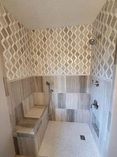 Tiled shower with a bench seat. Features diamond-patterned tile above wood-look tile, with silver fixtures against a light gray and beige palette.